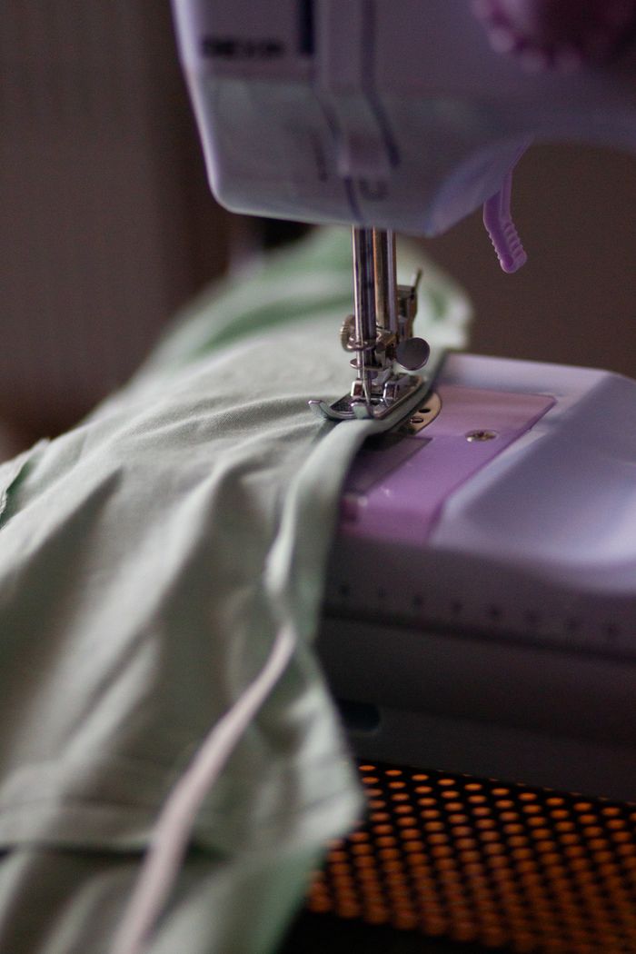 Detailed view of a sewing machine stitching light green fabric indoors.