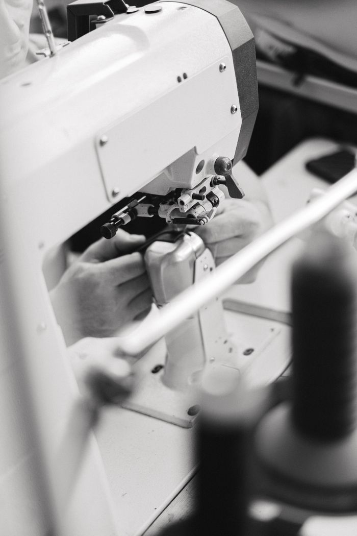 services-02 Black and white image of hands working with an industrial sewing machine.