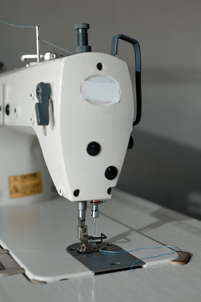 about-us-01 Detailed shot of a sewing machine focusing on the needle and thread mechanism.